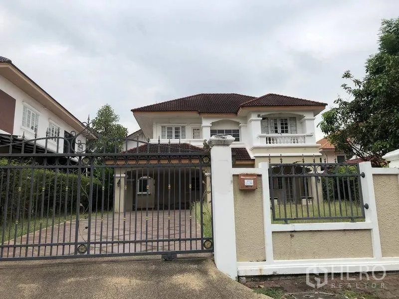 Detached House for rent or sale - Two-storey white detached house with brown tile roof, wrought-iron gate, gated driveway, and front lawn under cloudy sky.