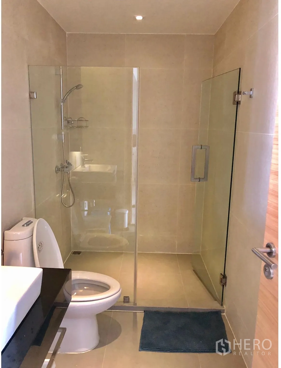 Condominium for rent in Watthana, Bangkok - Modern bathroom with glass-enclosed shower, beige tiles and toilet.