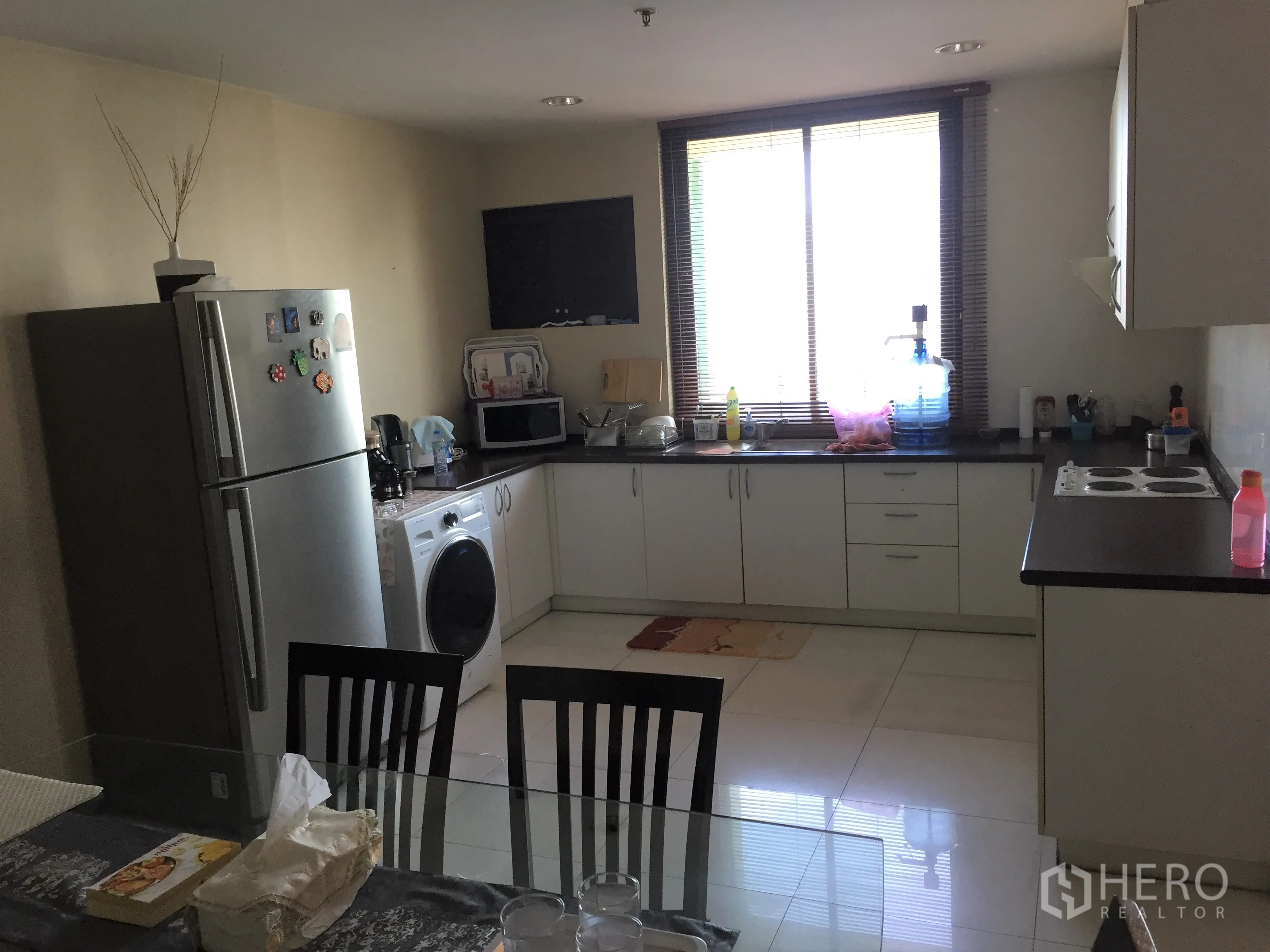Condominium for rent or sale in Khlong Toei, Bangkok - Bright kitchen with white cabinets, large window, fridge, washer and dining table in a Bangkok condominium.