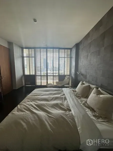 Condominium for rent or sale in Sathon, Bangkok - Primary bedroom with dark feature wall, king bed, and floor-to-ceiling windows with wooden blinds and city view.