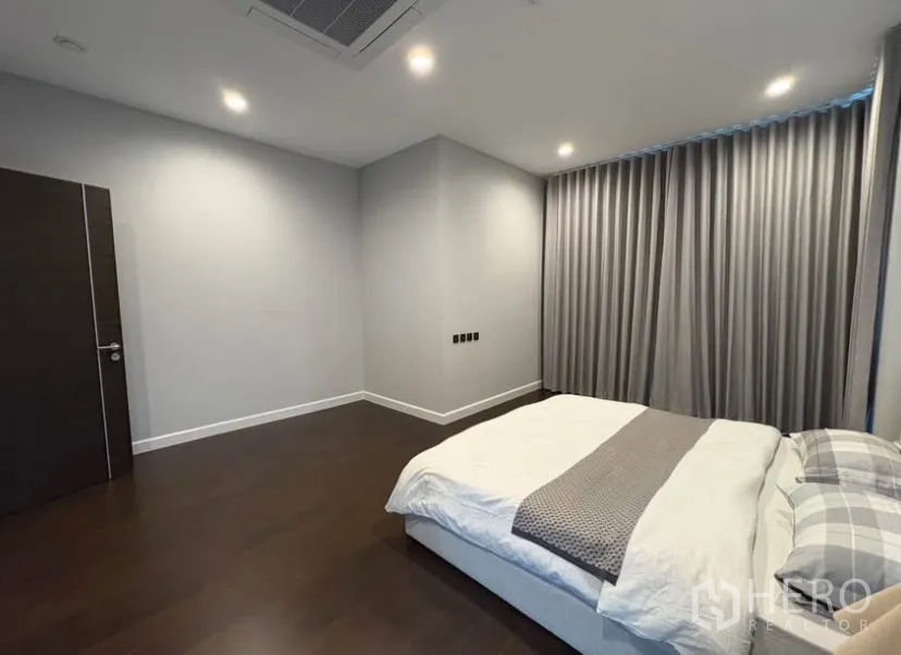 Detached House for rent in Suan Luang, Bangkok - Spacious bedroom with recessed lighting, dark wood floors and a king bed with gray drapes.