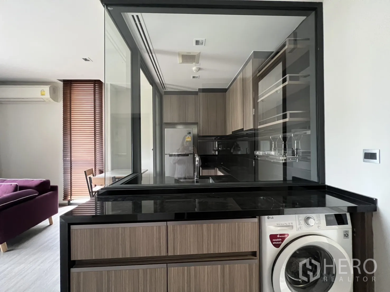 Condominium for rent in Watthana, Bangkok - Glass-partitioned kitchen looking into a living area with a sofa and window blinds.