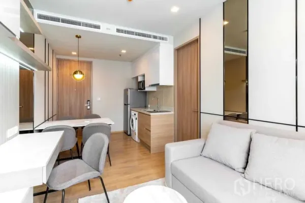 Condominium for rent in Watthana, Bangkok - Bright open-plan living area with kitchenette, dining table and gray sofa in a modern Bangkok condo.