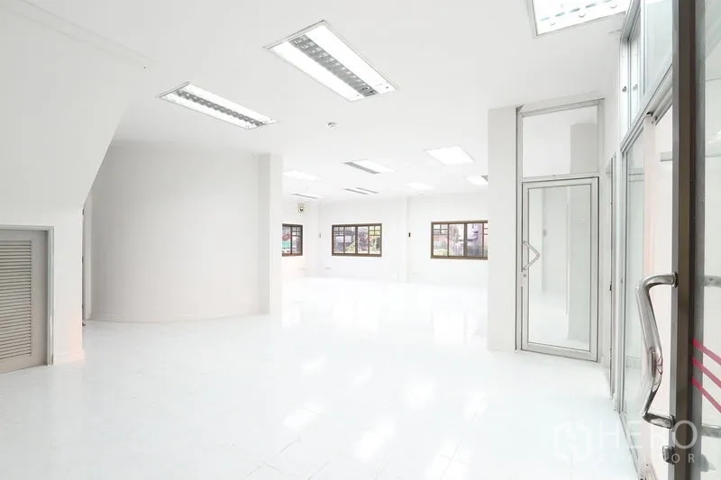 办公空间 出租在Bang Na, Bangkok - 一层纯白办公区，大窗与日光灯，玻璃门入口。