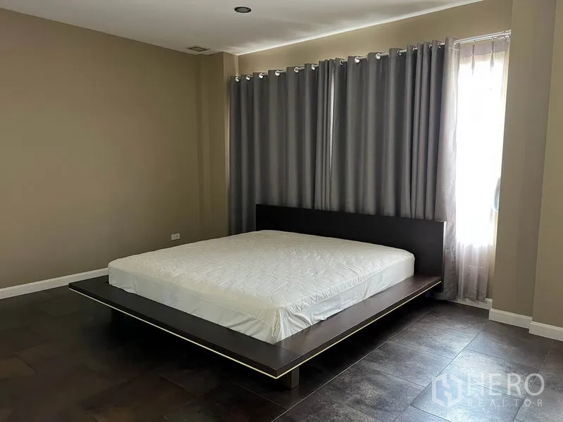 Detached House for rent in Bang Kapi, Bangkok - Primary bedroom with platform bed, full-length curtains and tiled flooring.