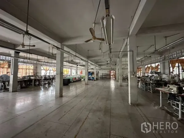 Warehouse for rent in Rat Burana, Bangkok - Open factory hall with concrete columns, ceiling fans, and workstations along the sides.