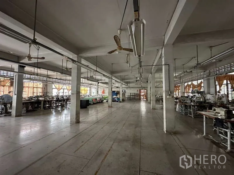 Warehouse for rent in Rat Burana, Bangkok - Open factory hall with concrete columns, ceiling fans, and workstations along the sides.
