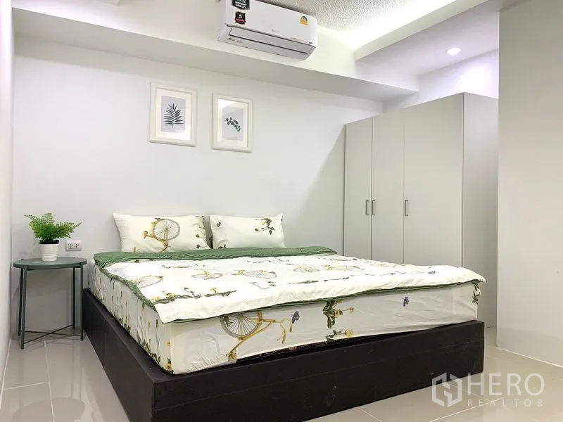 คอนโด ให้เช่าหรือขายในKhlong Toei, Bangkok - ห้องนอนติดแอร์ เตียงคู่ ตู้เสื้อผ้าสีขาว และโต๊ะข้าง เต็มไปด้วยโทนสีอบอุ่น