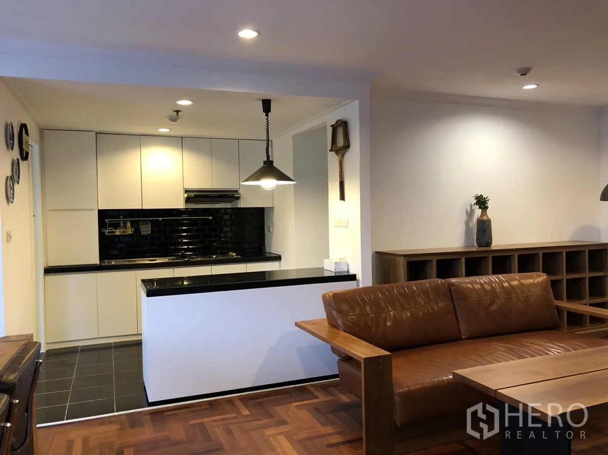 คอนโด ให้เช่าในWatthana, Bangkok - ห้องรับแขกเชื่อมครัว โซฟาหนัง พื้นไม้ และครัวสีขาวแบ็กสเปลชกระเบื้องสีดำ
