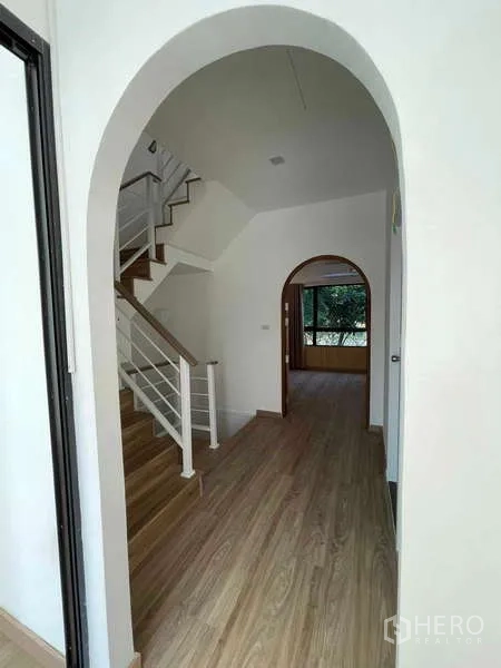 Townhouse for rent or sale in Bang Kapi, Bangkok - Corridor with arched doorway and staircase with white railing and wooden steps.
