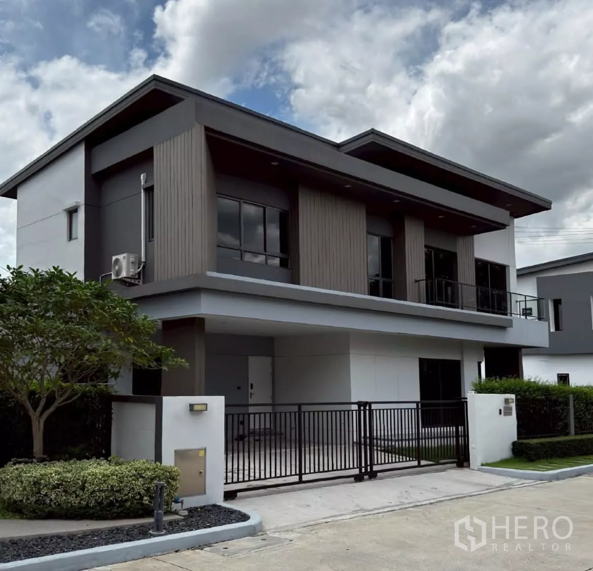 บ้าน ให้เช่าหรือขายในLat Krabang, Bangkok - มุมมองเฉียงของบ้าน 2 ชั้นสมัยใหม่ ประตูรั้วเหล็กสีดำ ที่จอดรถในร่ม และหน้าบ้านเรียบหรู.