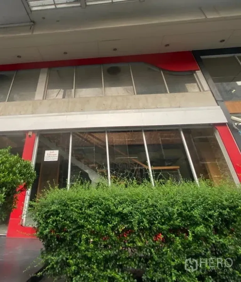 零售空间 出租在Pathum Wan, Bangkok - 街铺外立面，大片玻璃橱窗与红色装饰，前方有绿篱。