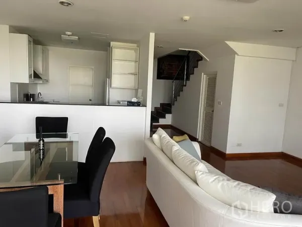 公寓 出租在Pathum Wan, Bangkok - 开放式客餐厅，玻璃餐桌、白色沙发与紧凑厨房，并设室内楼梯。