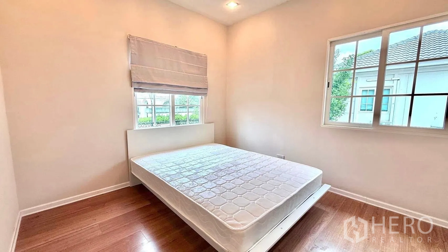Detached House for rent or sale in Bueng Kum, Bangkok - Cozy bedroom with a queen bed, wood flooring and two windows bringing in natural light.