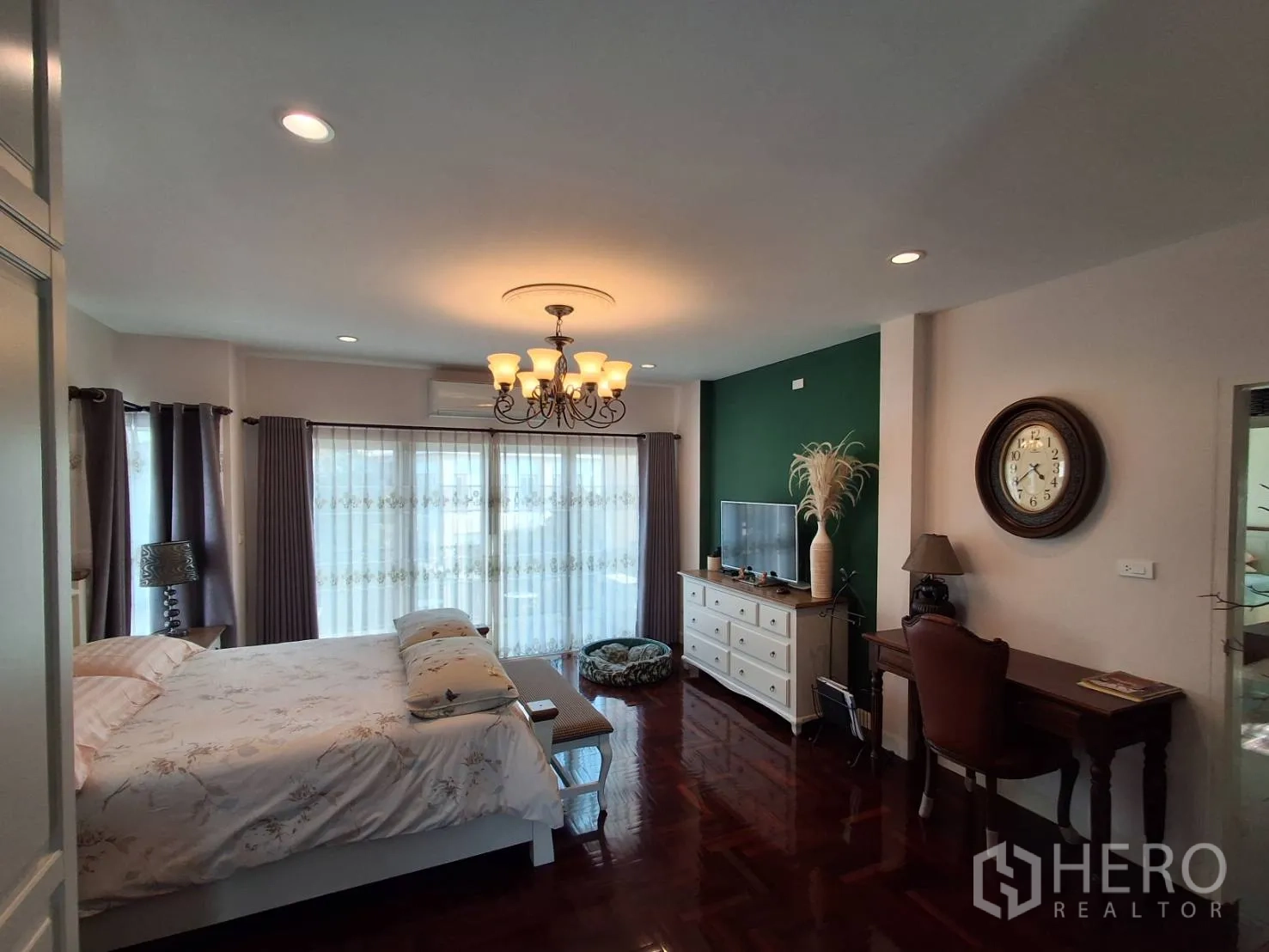 Detached House for rent or sale in Ban Chang, Rayong - Spacious master bedroom with chandelier, sheer curtains, TV console, desk, air conditioner and polished wood floor.