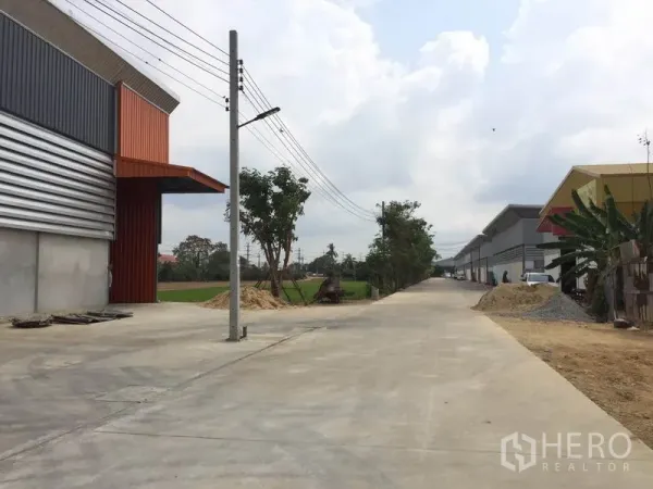 Warehouse for rent in Sai Noi, Nonthaburi - Long concrete access road through the industrial estate with utilities and green fields nearby.