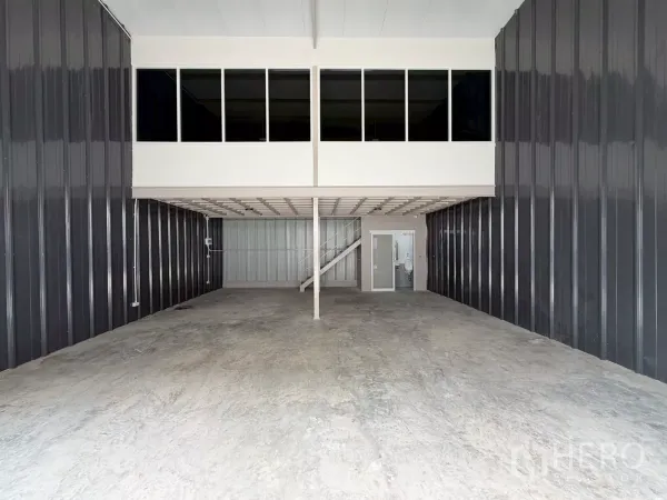 货栈 出租在Suan Luang, Bangkok - 仓库内部，高挑空间，带窗夹层办公室，混凝土地面与卷闸入口。