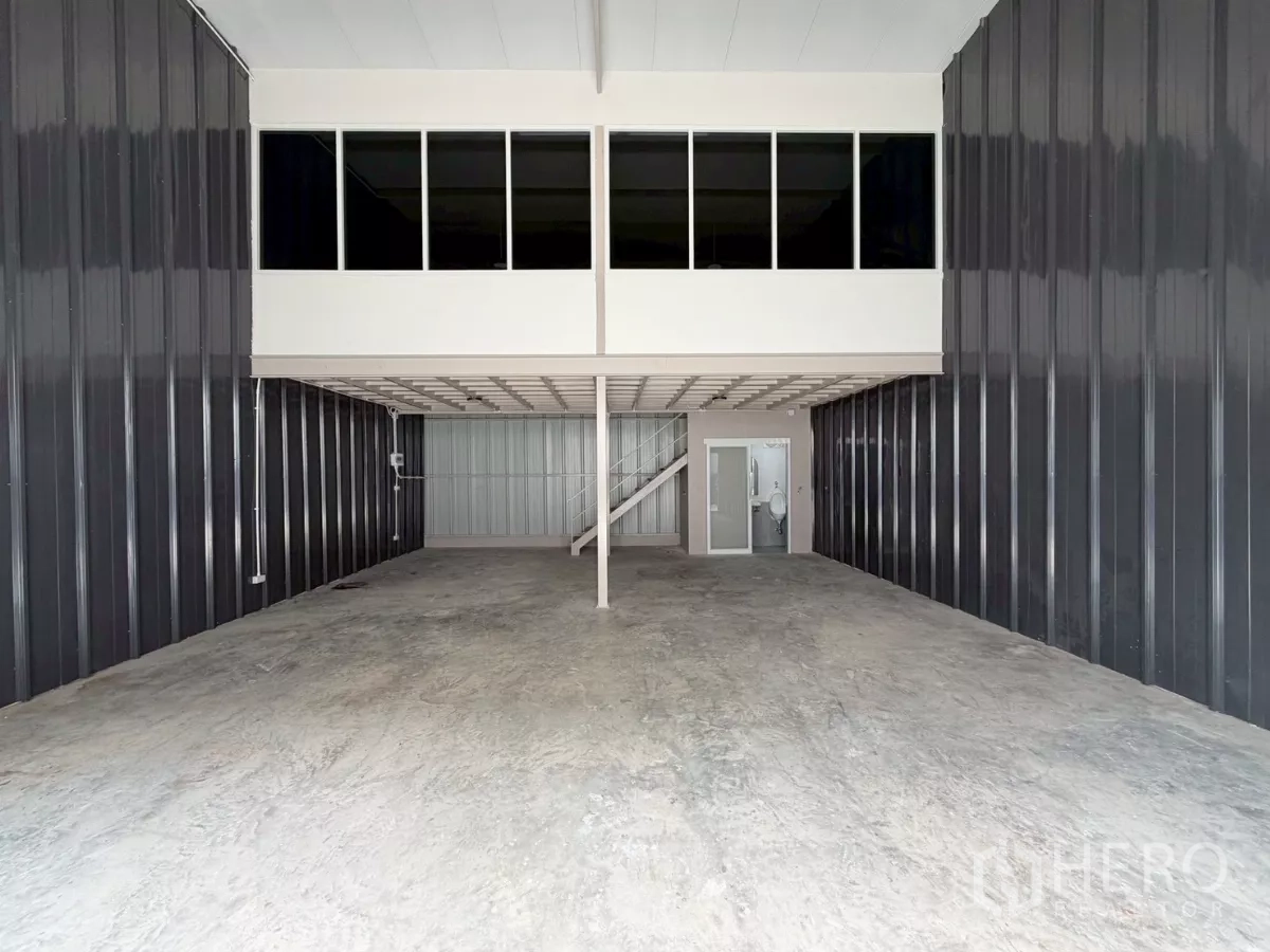 货栈 出租在Suan Luang, Bangkok - 仓库内部，高挑空间，带窗夹层办公室，混凝土地面与卷闸入口。