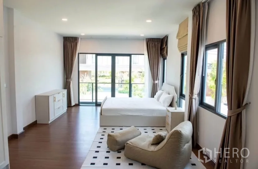Detached House for rent in Bang Phli, Samut Prakan - Spacious master bedroom with large windows, balcony doors and a lounge chair.