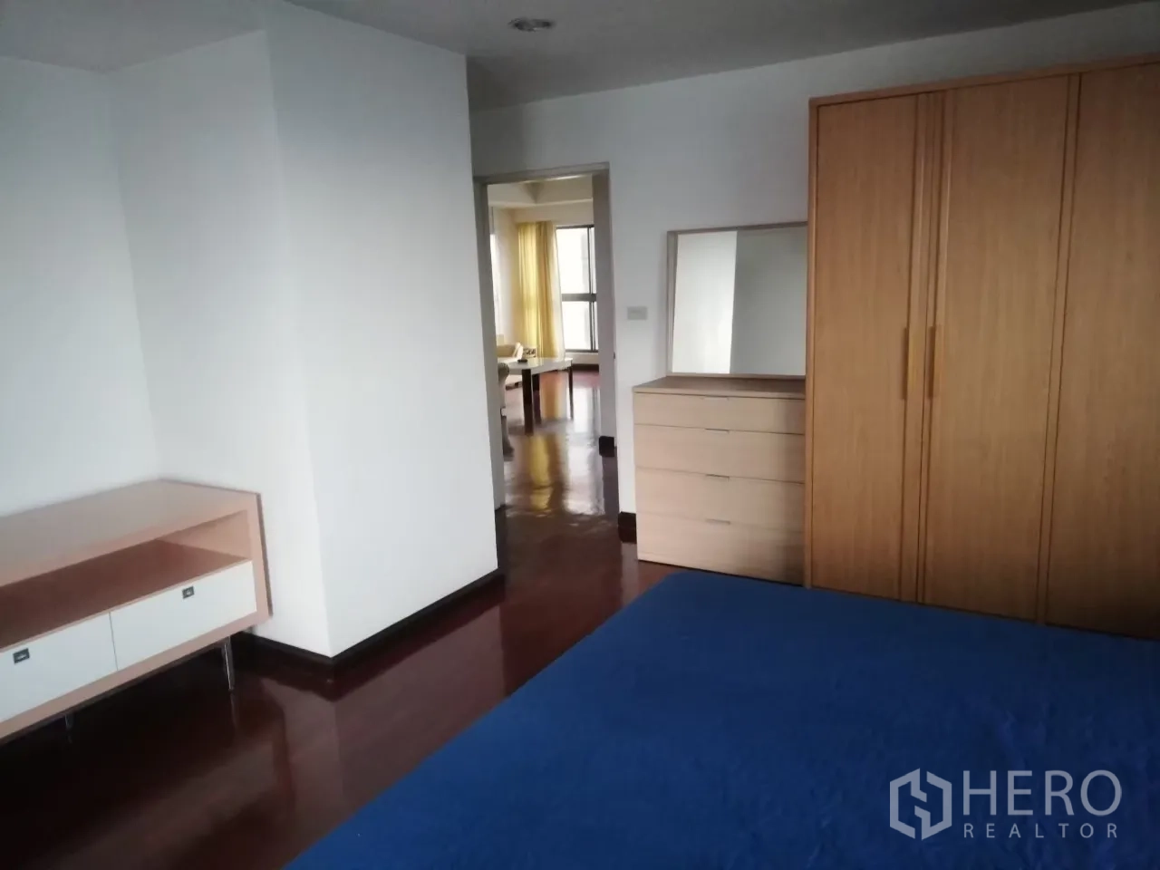 คอนโด ให้เช่าในPhaya Thai, Bangkok - ห้องนอนหลักพร้อมผ้าปูเตียงสีน้ำเงิน ตู้เสื้อไม้ และพื้นไม้ขัดมันวาวต่อเนื่องไปยังโซนรับแขก