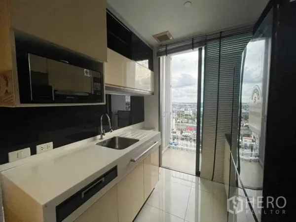 Condominium for sale - Compact modern kitchen with white countertop, glossy cabinets, and balcony door to a city view.