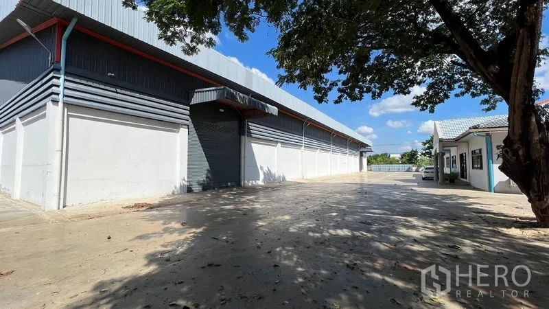 Warehouse for rent in Thanyaburi, Pathum Thani - Side view of warehouse showing roller shutter loading door and long driveway.