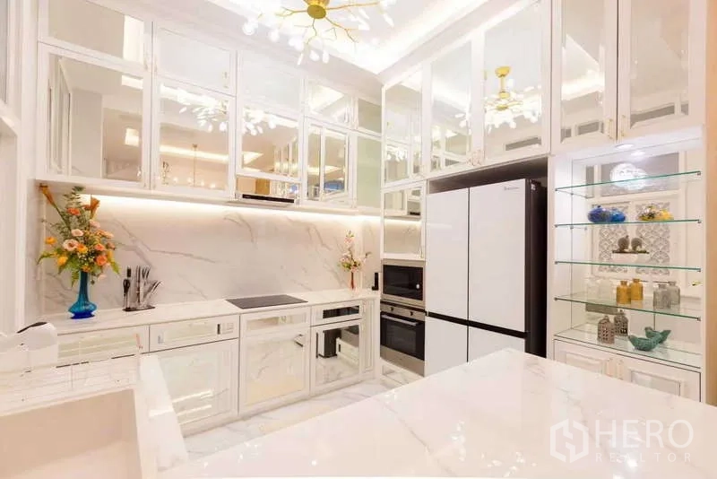 Townhouse for rent in Lat Phrao, Bangkok - Modern white marble kitchen with mirrored cabinets and built-in appliances.