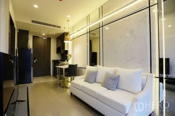 公寓 出租在Watthana, Bangkok - 开放式起居区，沙发、双人餐桌与紧凑厨房，暖色灯光