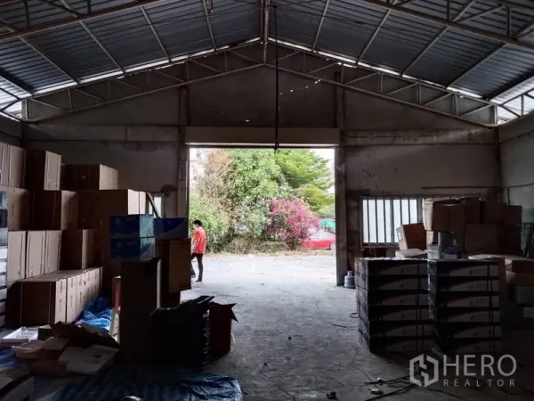 Warehouse for rent in Khlong Sam Wa, Bangkok - Open interior of the warehouse with steel truss roof, concrete floor and a large door facing greenery.
