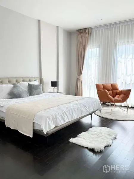 独立式住宅 出租或出售在Bang Phli, Samut Prakan - 明亮的主卧，软包床头、白色床品，落地窗旁有橙色躺椅。