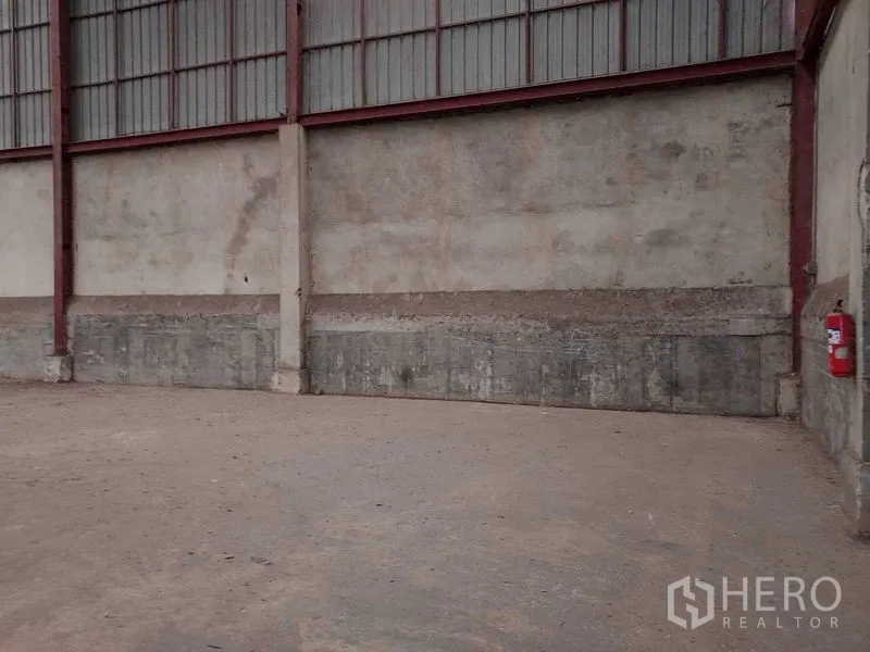 Warehouse for rent in Lat Lum Kaeo, Pathum Thani - Open storage bay along reinforced concrete wall with a visible fire extinguisher.