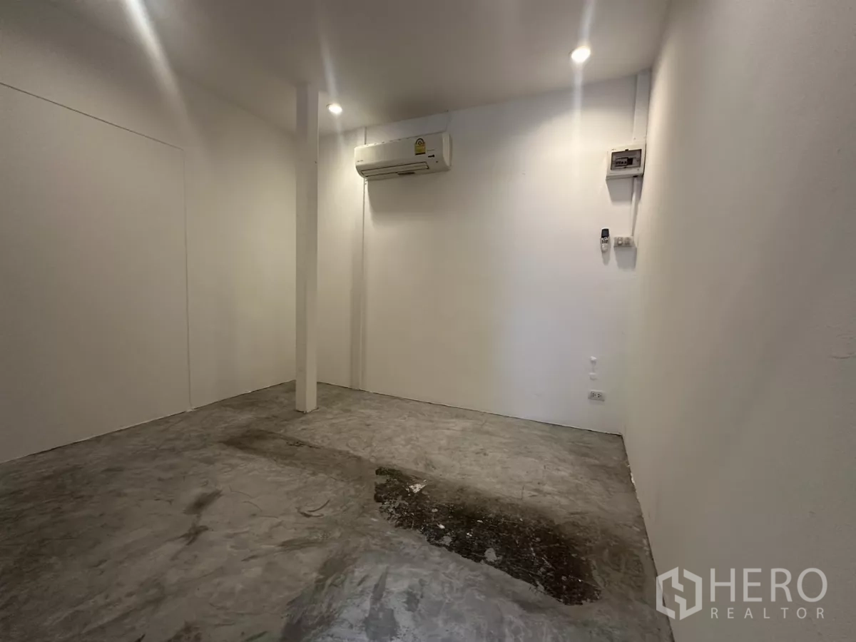 พื้นที่ขายปลีก ให้เช่า - พื้นที่ภายในขนาด 10 ตร.ม. ผนังสีขาว เสากลาง พื้นคอนกรีต ไฟสปอตไลท์ และแอร์แบบติดผนัง