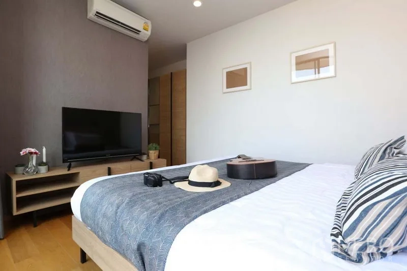 Condominium for sale in Bang Rak, Bangkok - Second bedroom with TV console, air conditioner and neatly dressed bed.