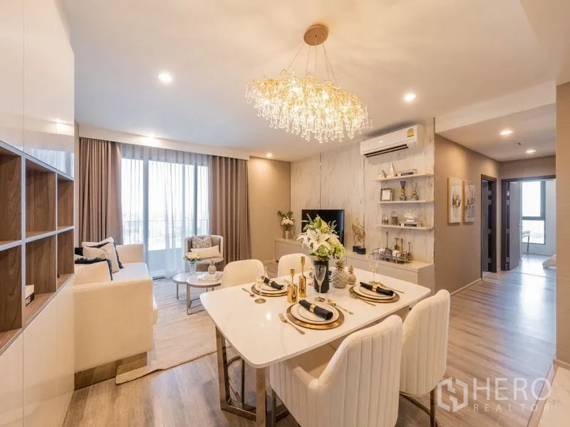 Condominium for rent in Bang Na, Bangkok - Open-plan living and dining area with crystal chandelier, soft neutral decor and large windows.
