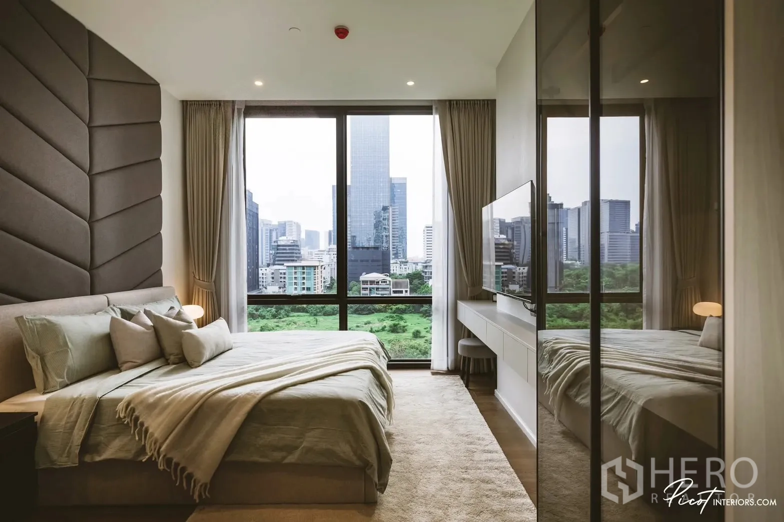 Condominium for rent in Pathum Wan, Bangkok - Primary bedroom with full-height windows, park and skyline views, wall-mounted TV and desk.