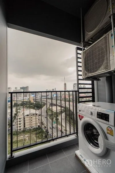 Condominium for rent - Covered balcony with washing machine and AC units overlooking the Rama 9 city skyline.
