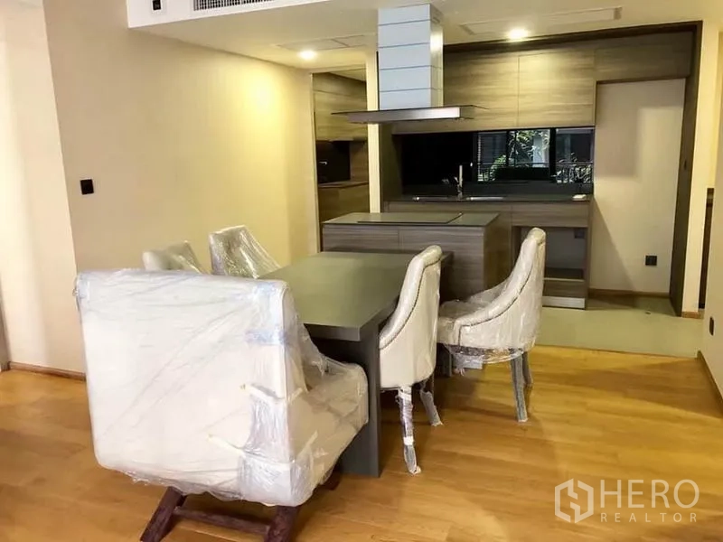Condominium for rent in Pathum Wan, Bangkok - Open-plan dining area and island kitchen with wood cabinets, range hood and warm lighting.