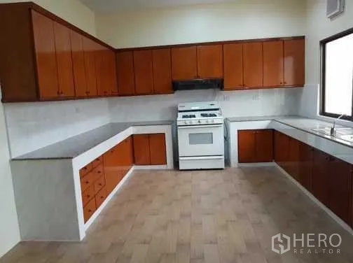 Townhouse for rent in Khlong Toei, Bangkok - L-shaped kitchen with stone countertops, white stove and ample cabinets.