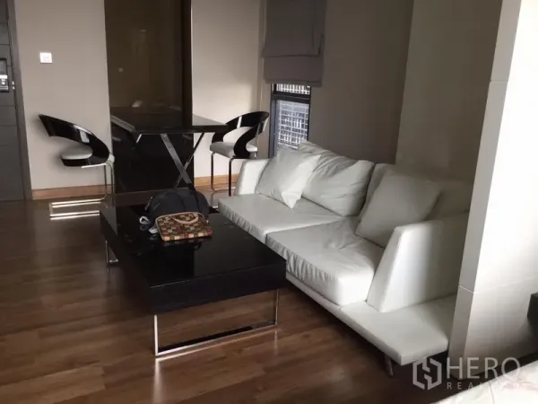 Condominium for rent in Huai Khwang, Bangkok - Contemporary living area with white sofa, glossy black coffee table and two-seat dining set.