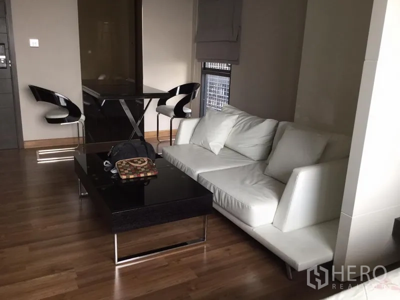 Condominium for rent in Huai Khwang, Bangkok - Contemporary living area with white sofa, glossy black coffee table and two-seat dining set.