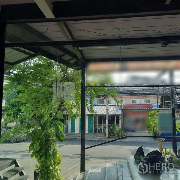 零售空间 出租在Lat Phrao, Bangkok - 透过店面玻璃可见街景、绿树与周边小店。