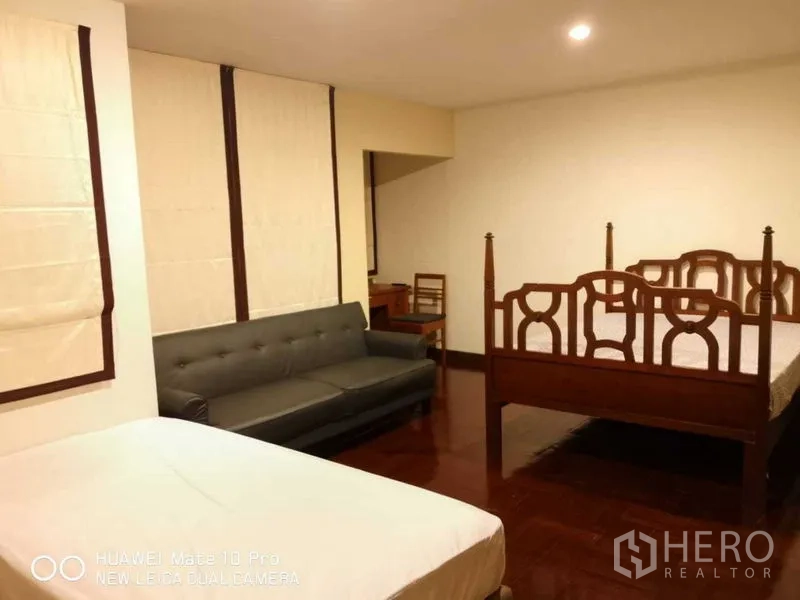 Townhouse for rent or sale in Suan Luang, Bangkok - Spacious bedroom with multiple beds, sofa and warm lighting on wooden floors.