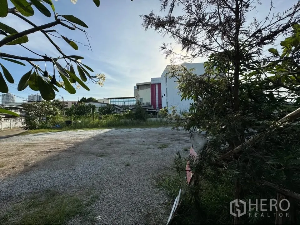 Land for rent in Bang Na, Bangkok - Open plot with compacted ground, surrounding greenery, and nearby commercial buildings.