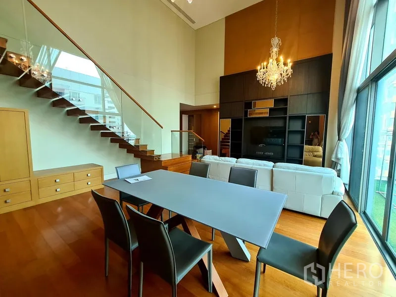 คอนโด ให้เช่าในKhlong Toei, Bangkok - พื้นที่นั่งเล่นและรับประทานอาหารแบบดูเพล็กซ์ พร้อมบันไดกระจก โคมระย้า โซฟาสีขาว และหน้าต่างสูงจรดเพดาน