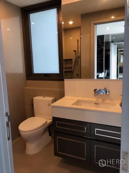 Condominium for rent in Khlong Toei, Bangkok - Modern bathroom featuring window, vanity, toilet and glass-enclosed shower.