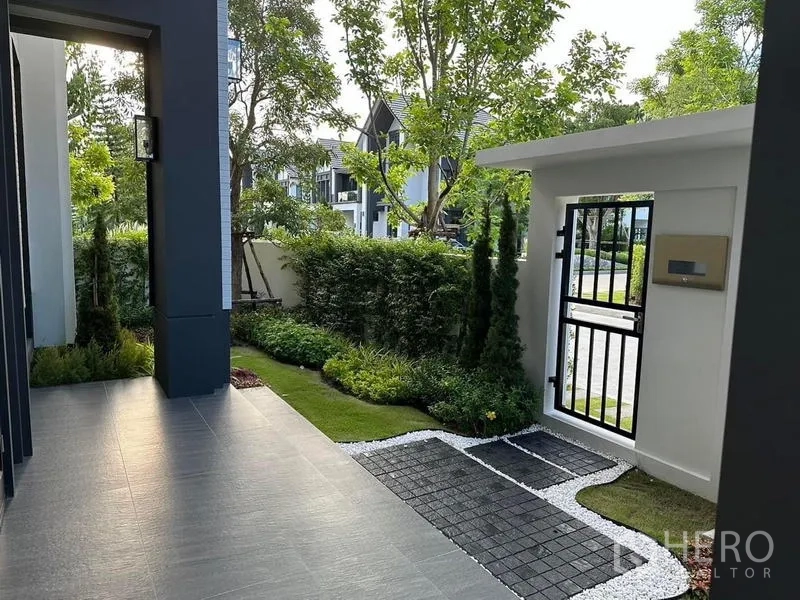 Detached House for rent or sale in Bang Phli, Samut Prakan - Front gate with black metal door, stepping-stone path and lush greenery around the entrance.