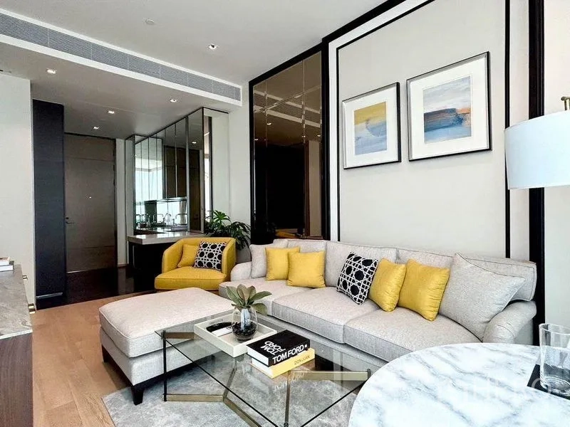 Condominium for rent in Pathum Wan, Bangkok - Open-plan living area with L-shaped sofa, glass coffee table and mirrored wall panels.