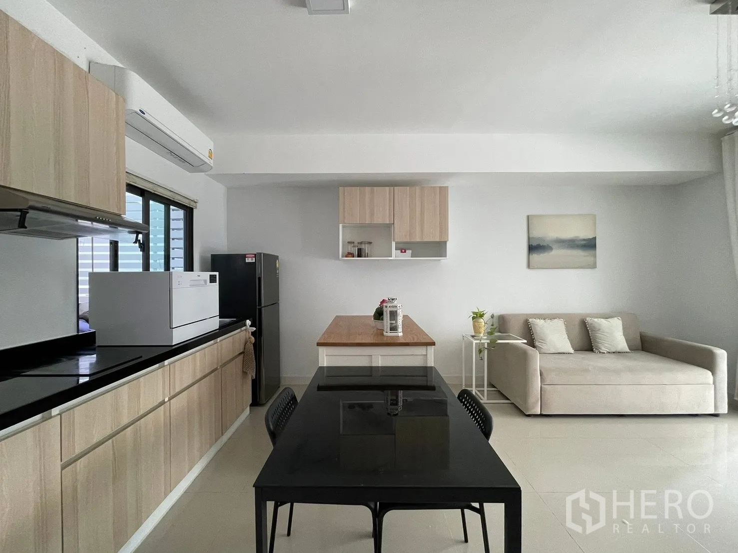 Townhouse for rent in Bang Phli, Samut Prakan - Open-plan kitchen with light wood cabinets, black countertop, dining table, and a beige sofa.
