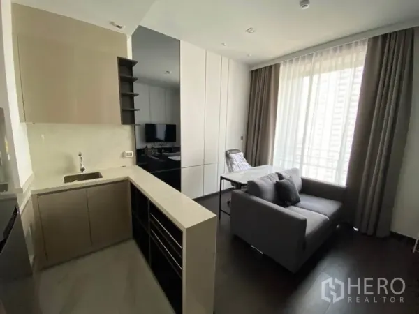 Condominium for rent in Watthana, Bangkok - Open-plan kitchen with L-shaped counter beside a bright living area and large city-view window.