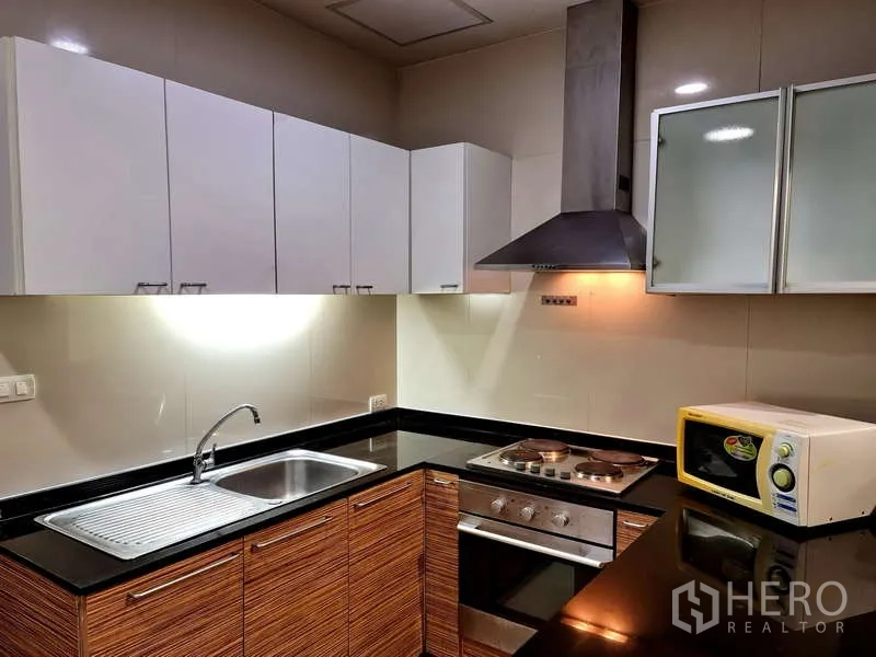 อพาร์ทเมนท์ ให้เช่า - ครัวรูปตัวแอล เคาน์เตอร์หินแกรนิตสีดำ อ่างล้างจาน เตาอบ ฮูดดูดควัน และตู้สีขาว
